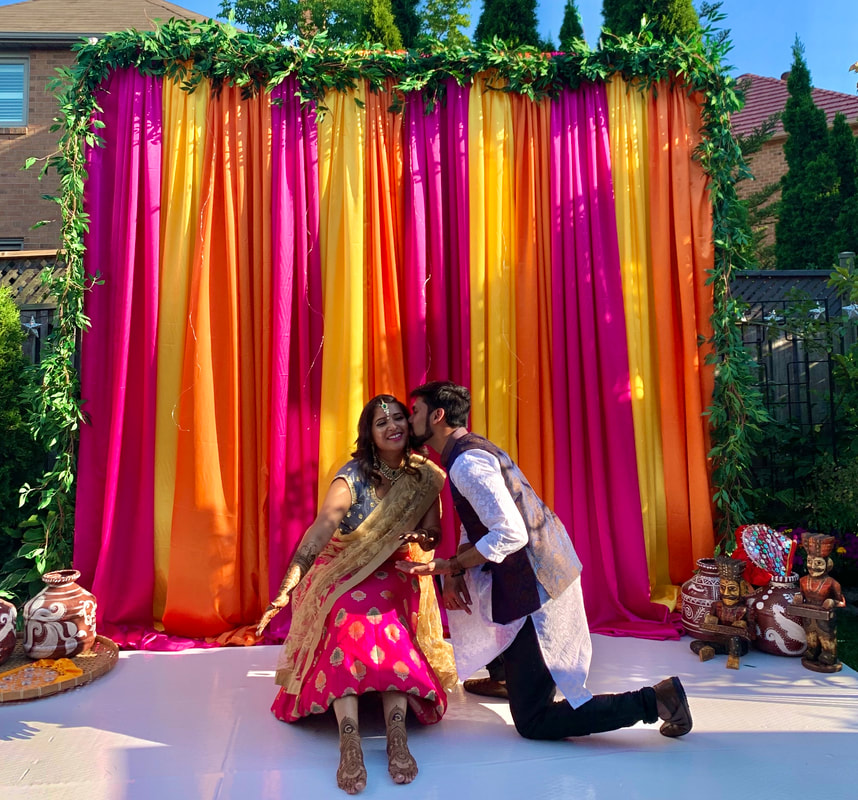 Groom giving his bride a kiss in front of a colourful sangeet backdrop