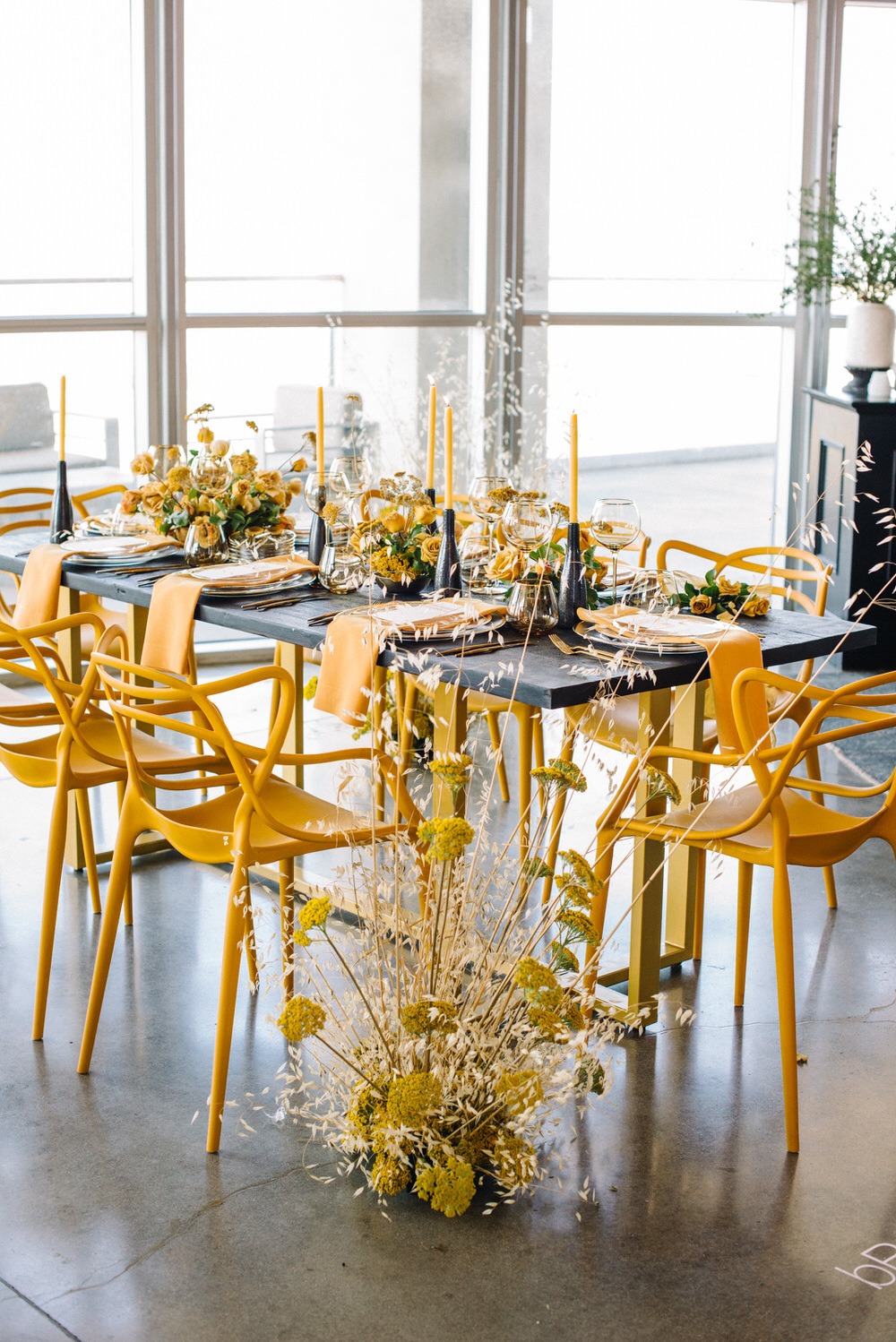 Architectural table design featuring yellow chairs and candles muted by black and gray table top decor. 
