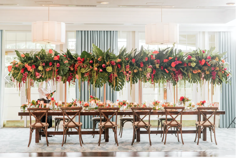 harvest table with overhead palm tree and bright floral canopy.