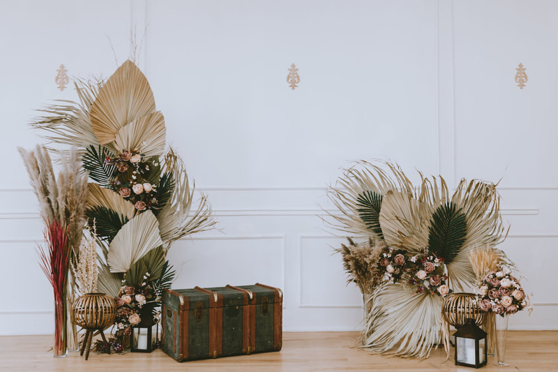 White wall at the wade studio framed by bohemian palm leaf arrangements with a green vintage trunk for seating